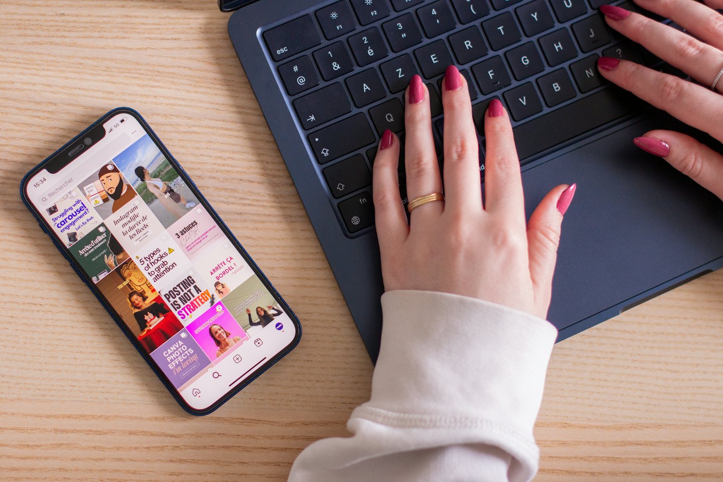 Hände mit pinken Nägeln tippen auf einem Laptop neben einem Smartphone.